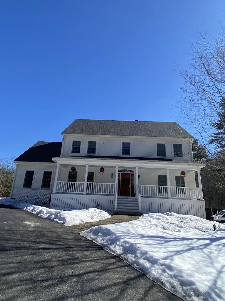 Snow-covered house with white porch and dark roof on a sunny day