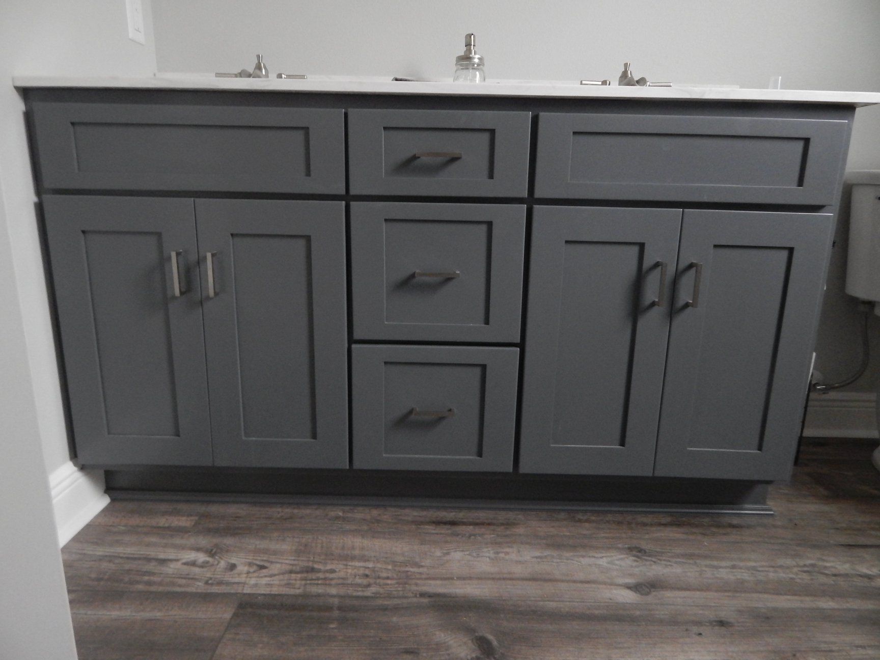 A bathroom vanity with gray cabinets and drawers next to a toilet.