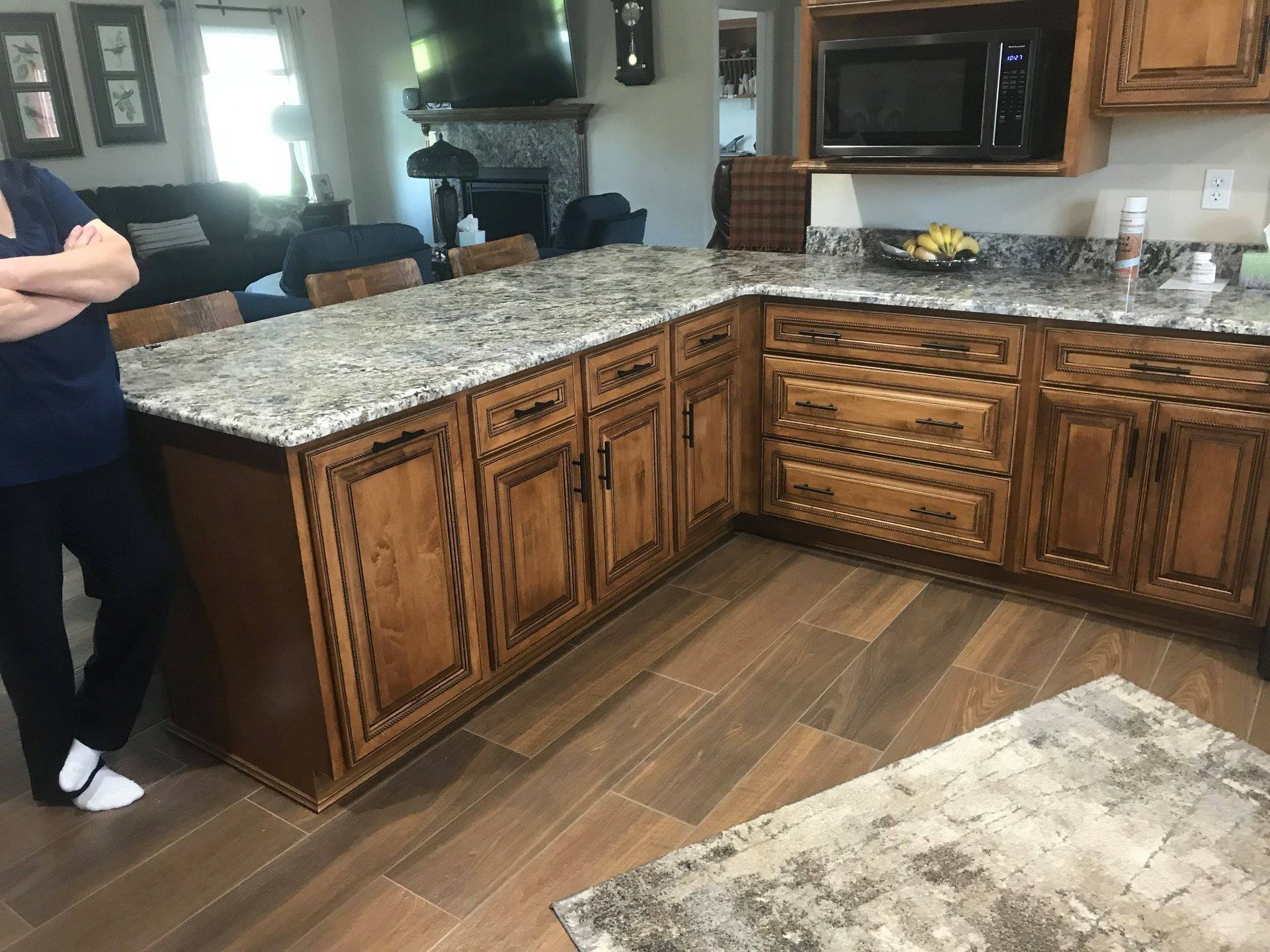 A woman is standing in a kitchen with wooden cabinets and granite counter tops.