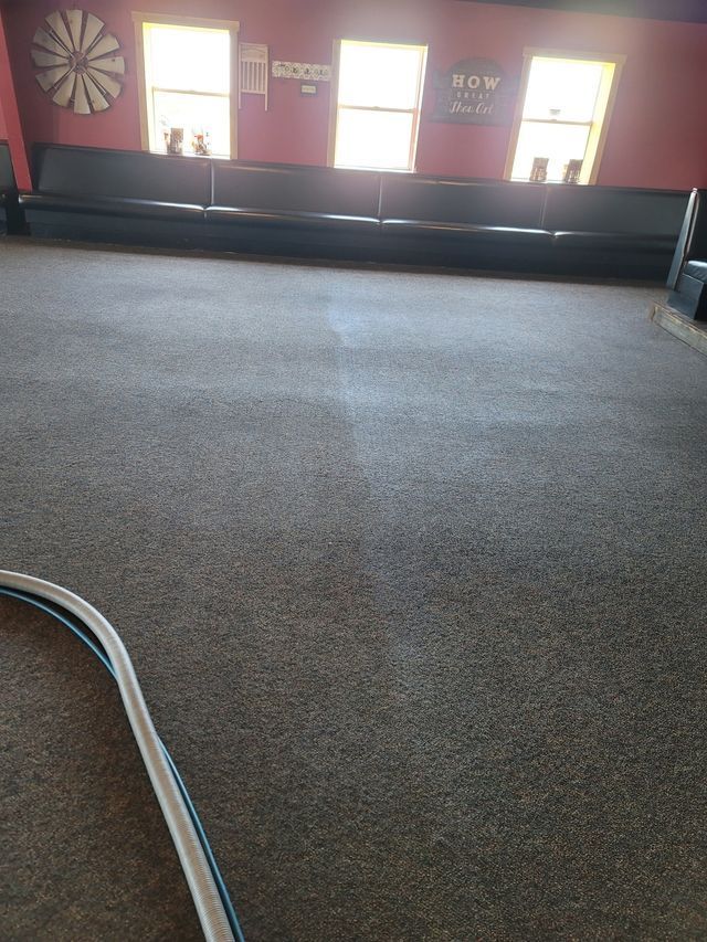 Empty indoor hall with carpeted floor, black railing, windows, and a dartboard on the wall