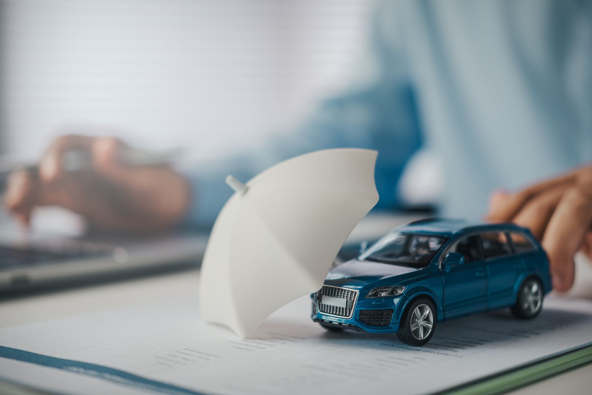 Small toy SUV protected by a umbrella on top of an open document, symbolizing car insurance or vehi