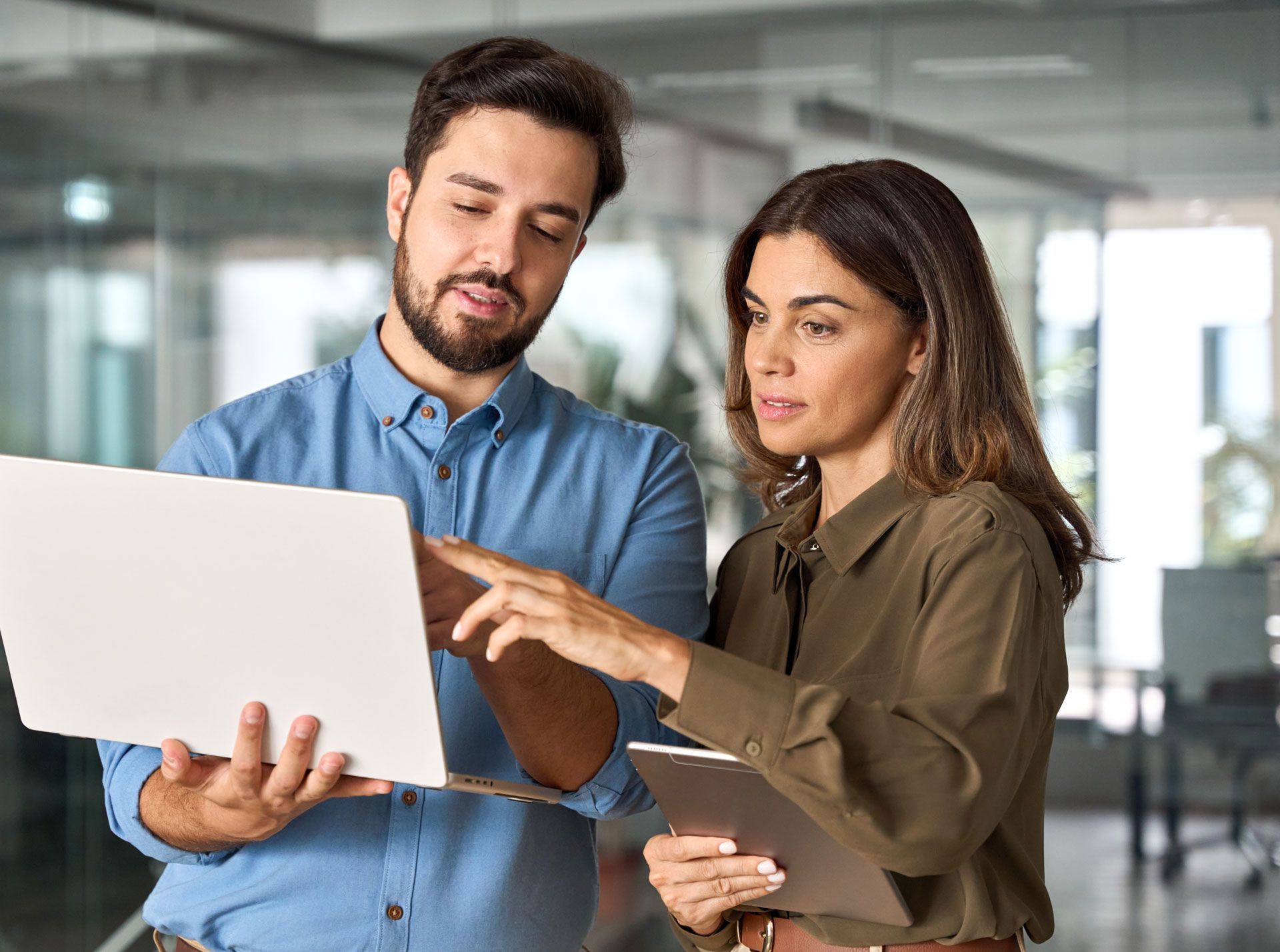 Man and woman looking at a laptop, pointing at the screen, in a modern office setting.
