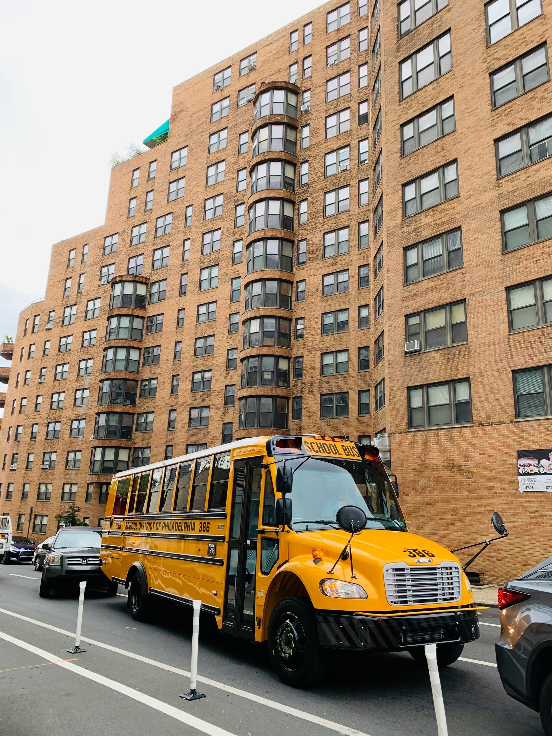 Yellow school bus parked on a city street in front of a tall brick apartment building.