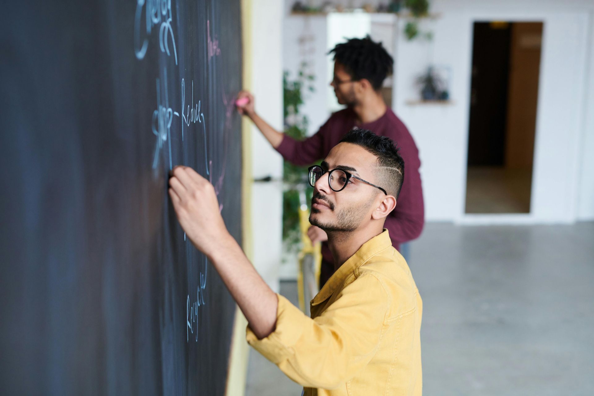 Two men are writing on a blackboard in a room.