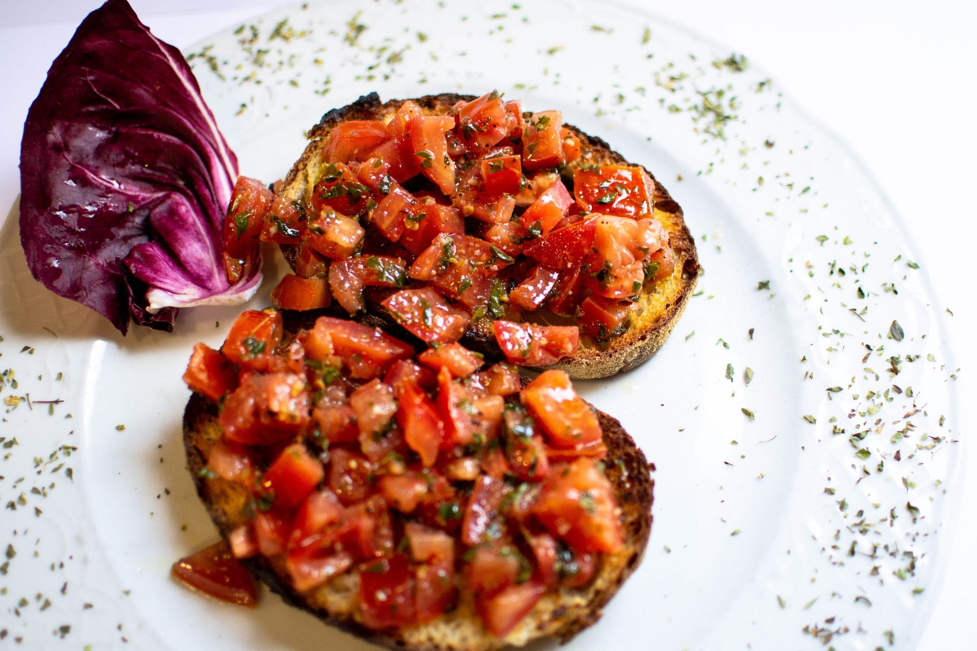 Two tomato bruschetta slices with red cabbage on a white plate, sprinkled with herbs.
