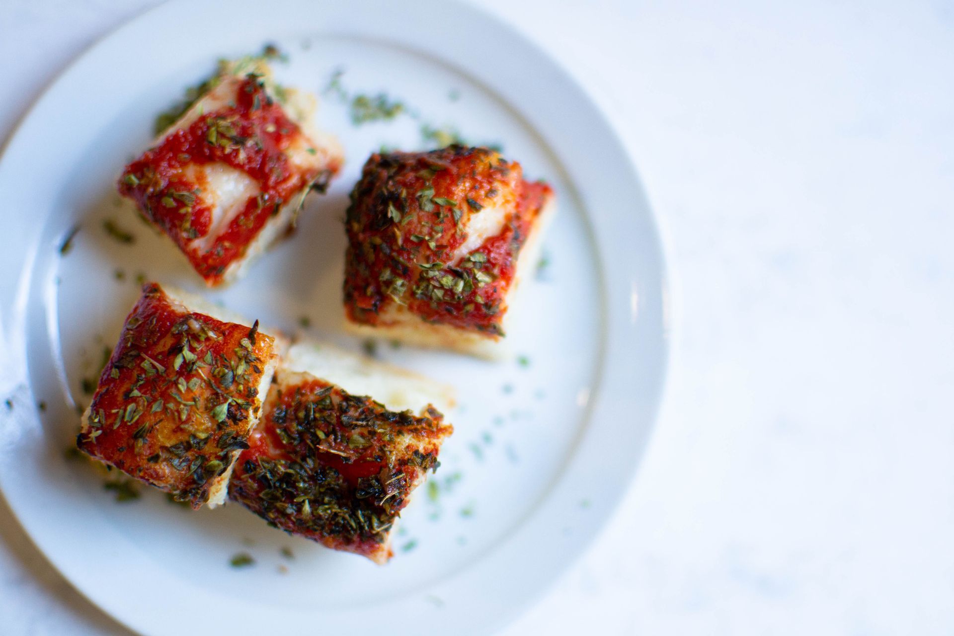 Three square slices of focaccia bread topped with tomato sauce and herbs on a white plate.
