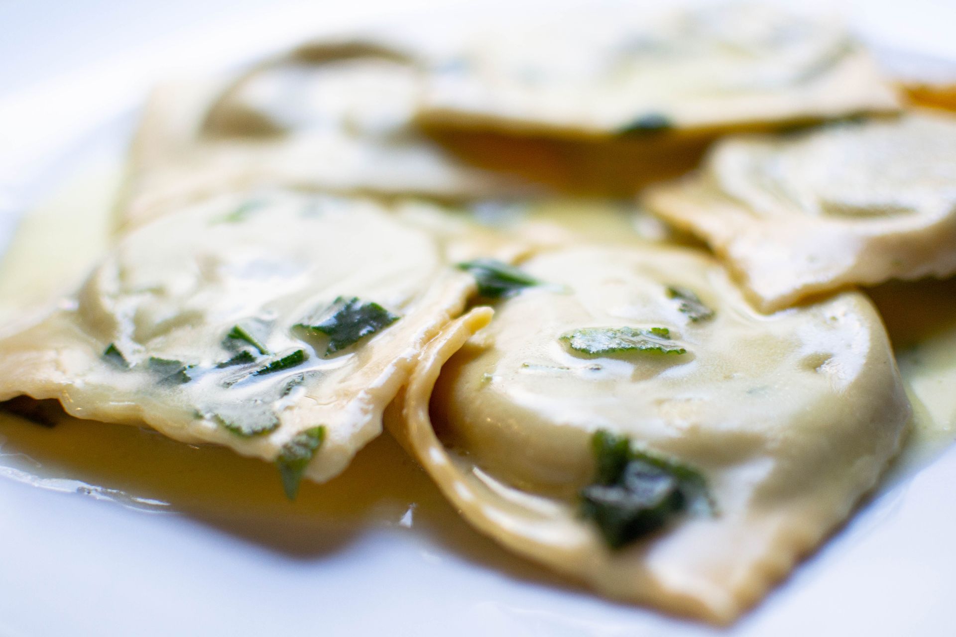 Ravioli with creamy white sauce and green herbs on a white plate.