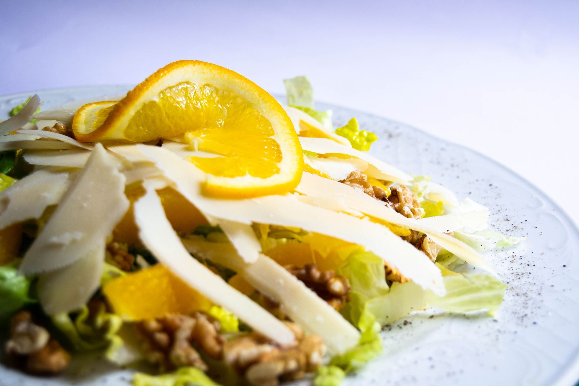 Salad with orange slices, shaved cheese, and walnuts on a white plate.