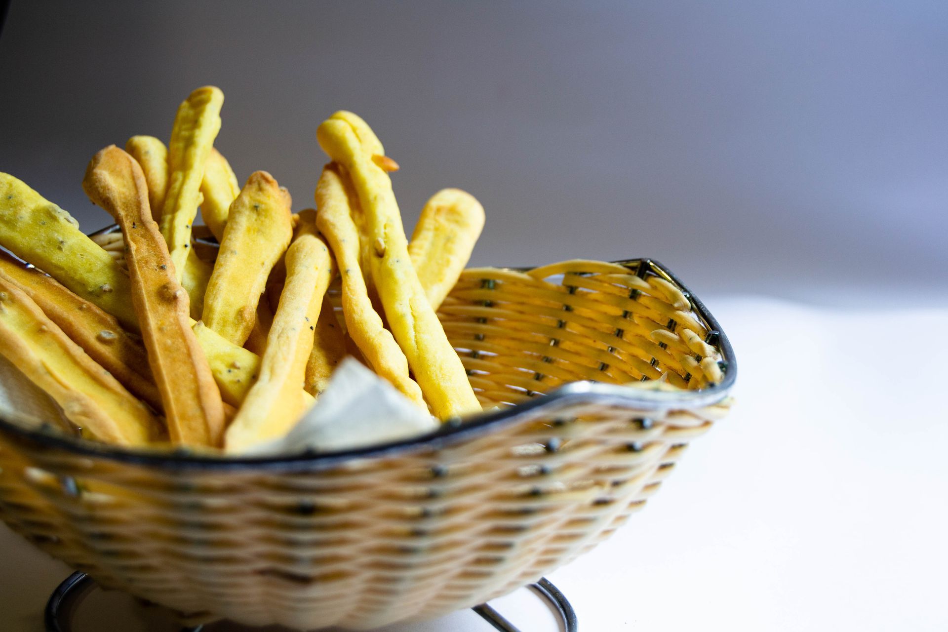 Basket of golden breadsticks, some with green herbs, on a white surface.