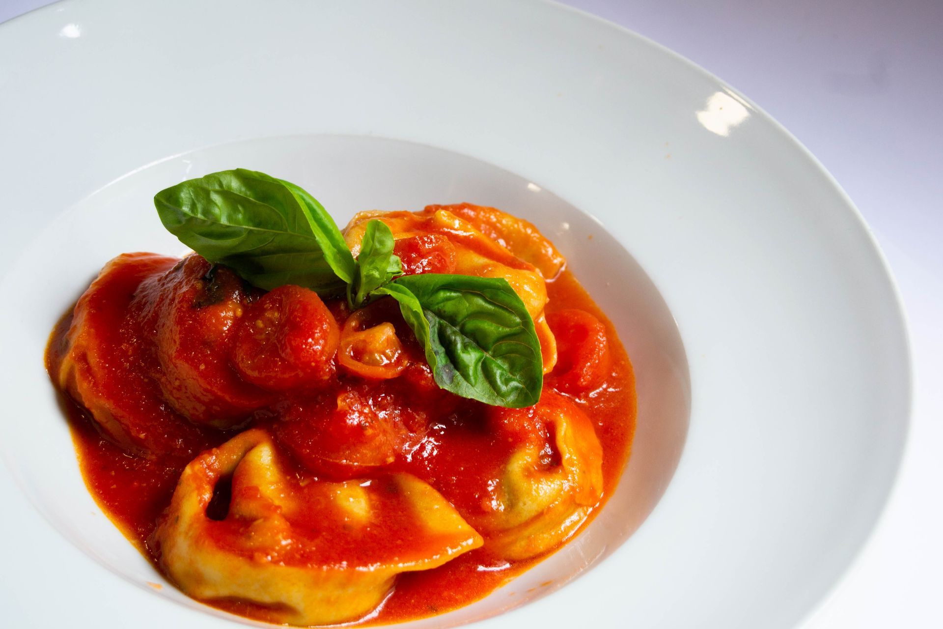 Pasta tortellini en salsa de tomate, adornada con albahaca en un recipiente blanco.