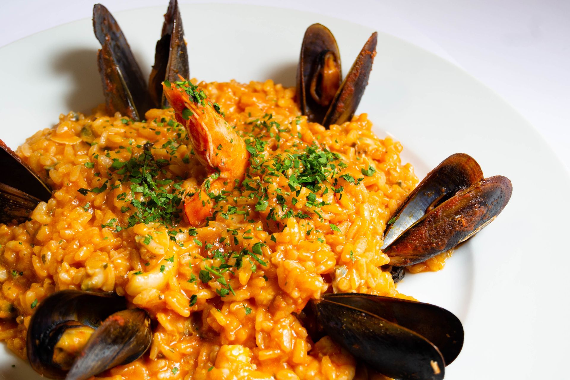 Seafood risotto: orange rice dish with shrimp, mussels, and chopped parsley, served on a white plate.