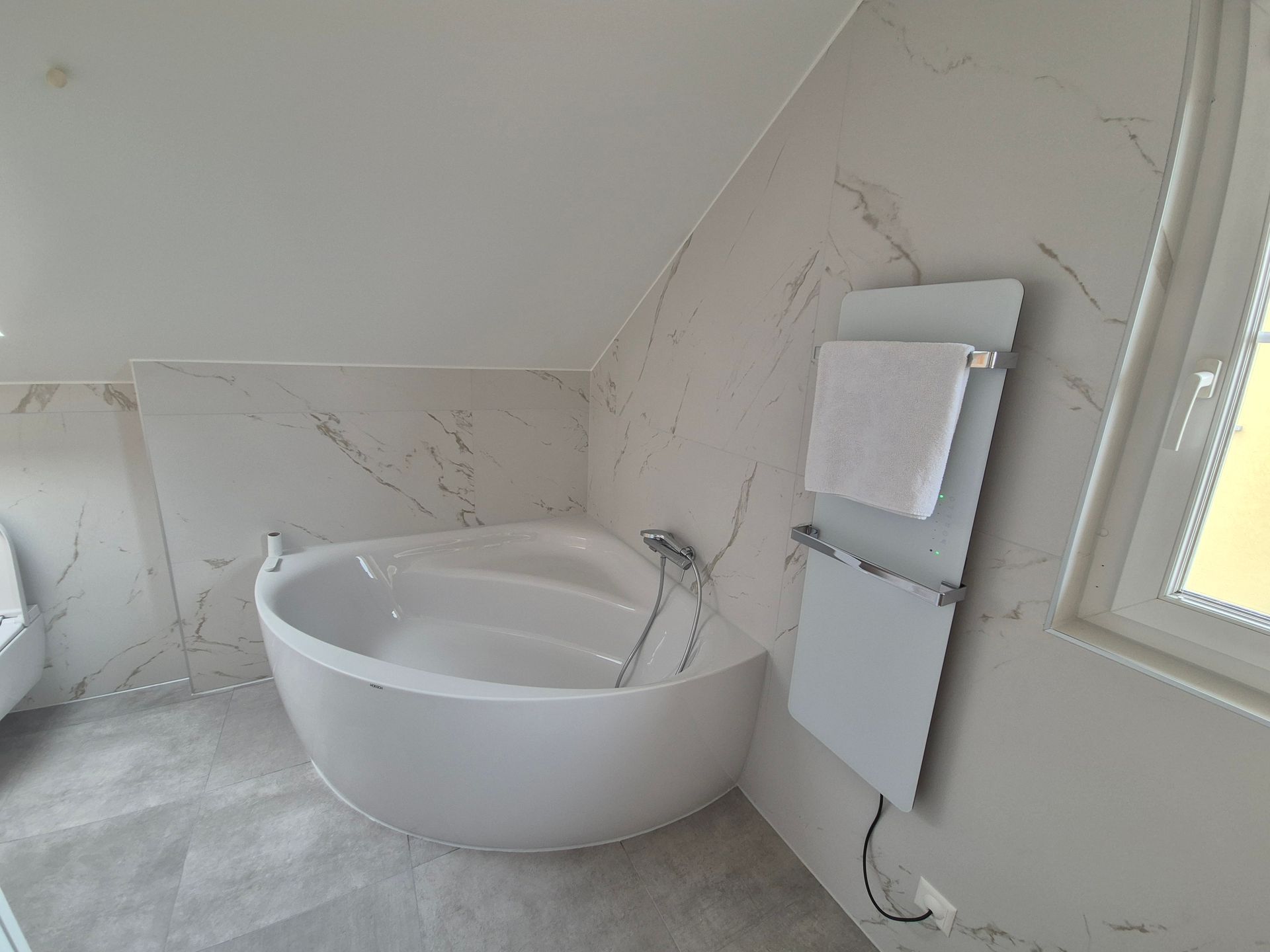 Baignoire blanche dans une salle de bains moderne avec carrelage mural imitation marbre et sèche-serviettes.