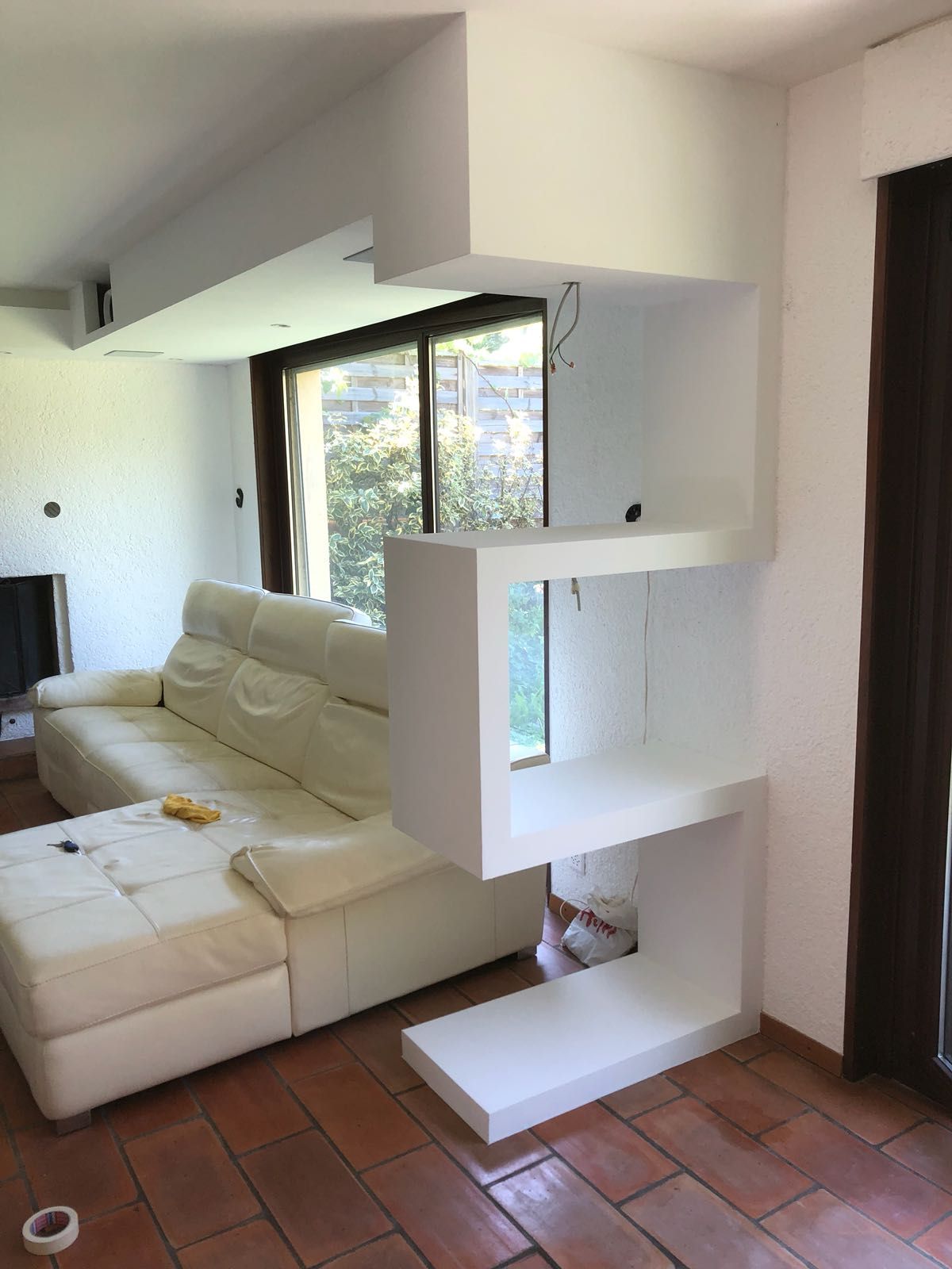 Étagère blanche en zigzag dans un salon moderne, à côté d'un canapé blanc et d'une fenêtre.