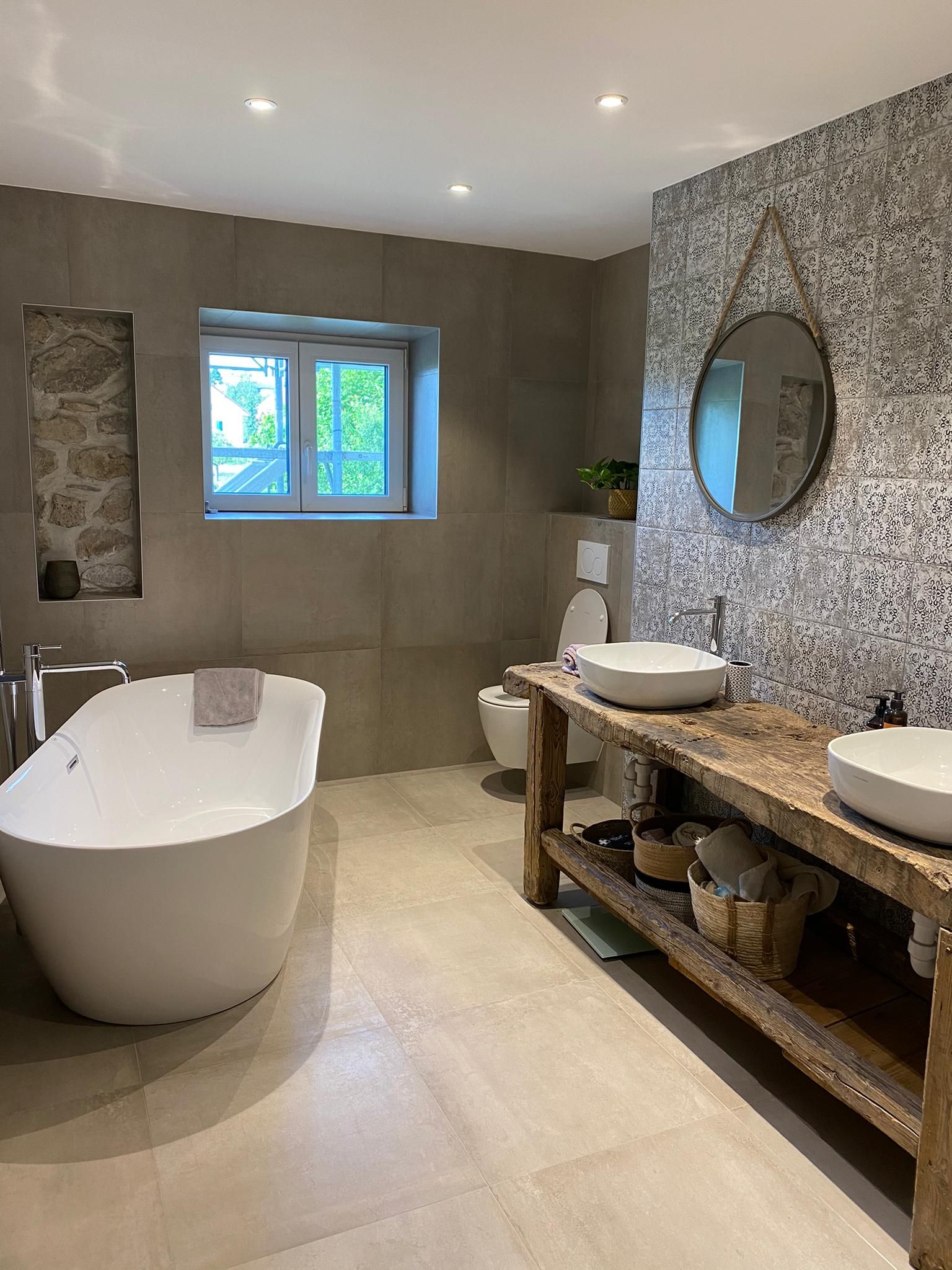 Salle de bains moderne avec baignoire blanche, meuble-lavabo en bois et mur en mosaïque.