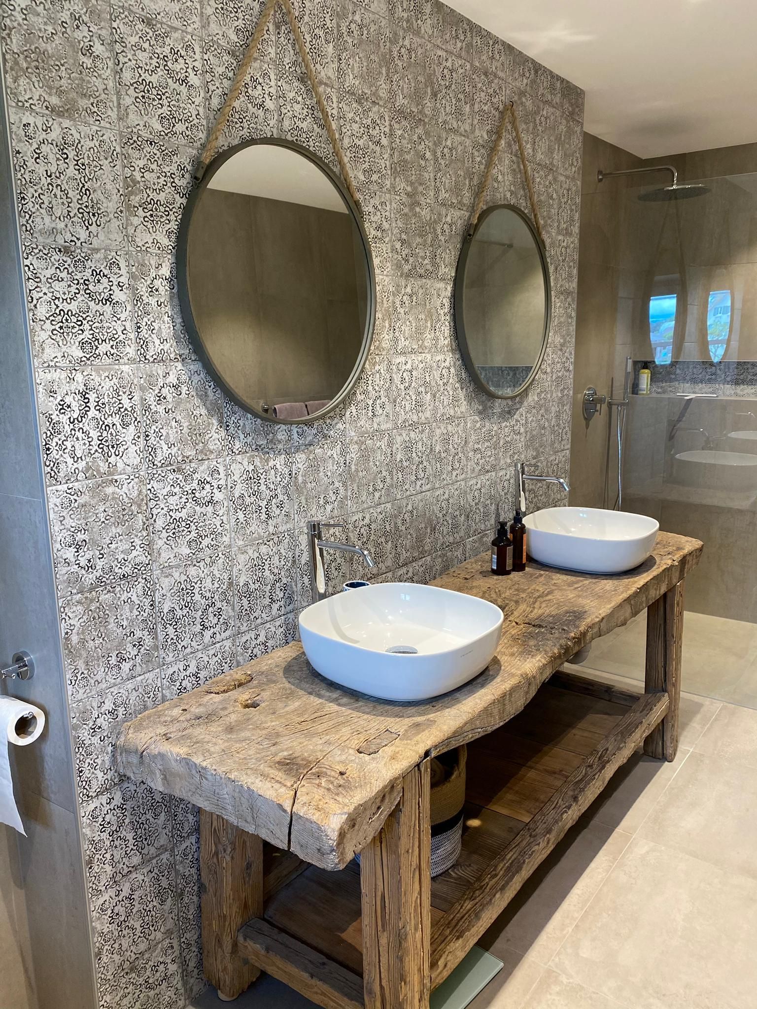 Salle de bains avec deux miroirs ronds, vasques à poser et meuble-lavabo rustique en bois. Crédence en carrelage à motifs.