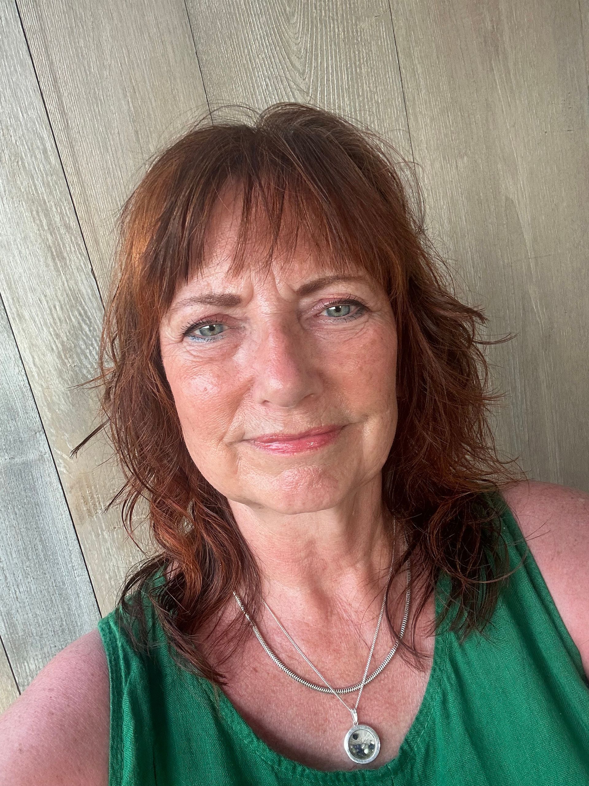 A woman with red hair is wearing a green tank top and a necklace.