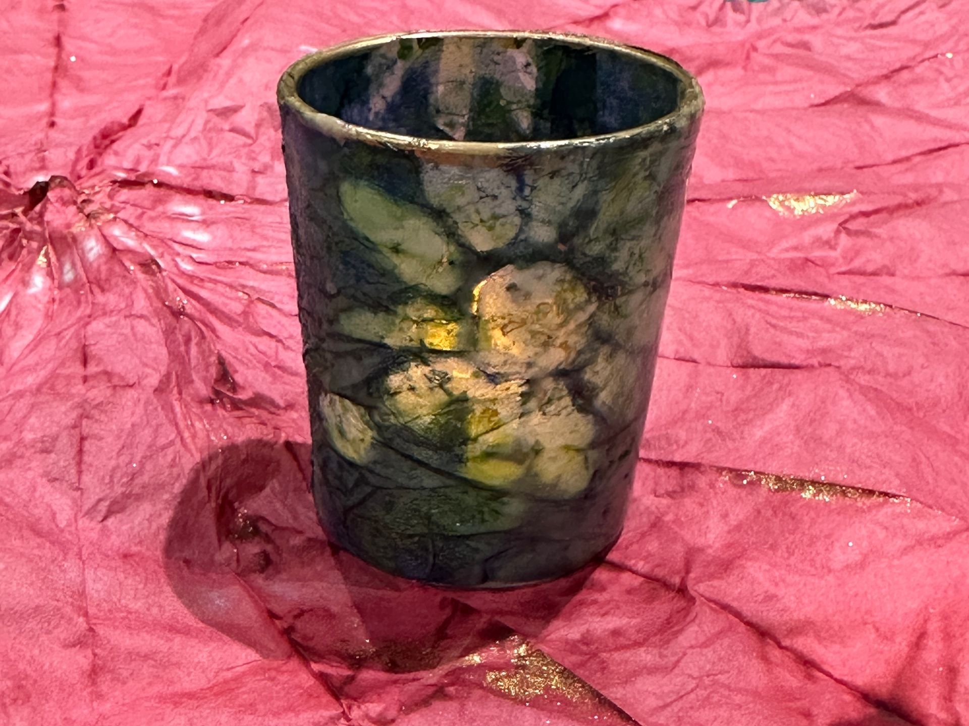 A green and yellow cup is sitting on a pink cloth.
