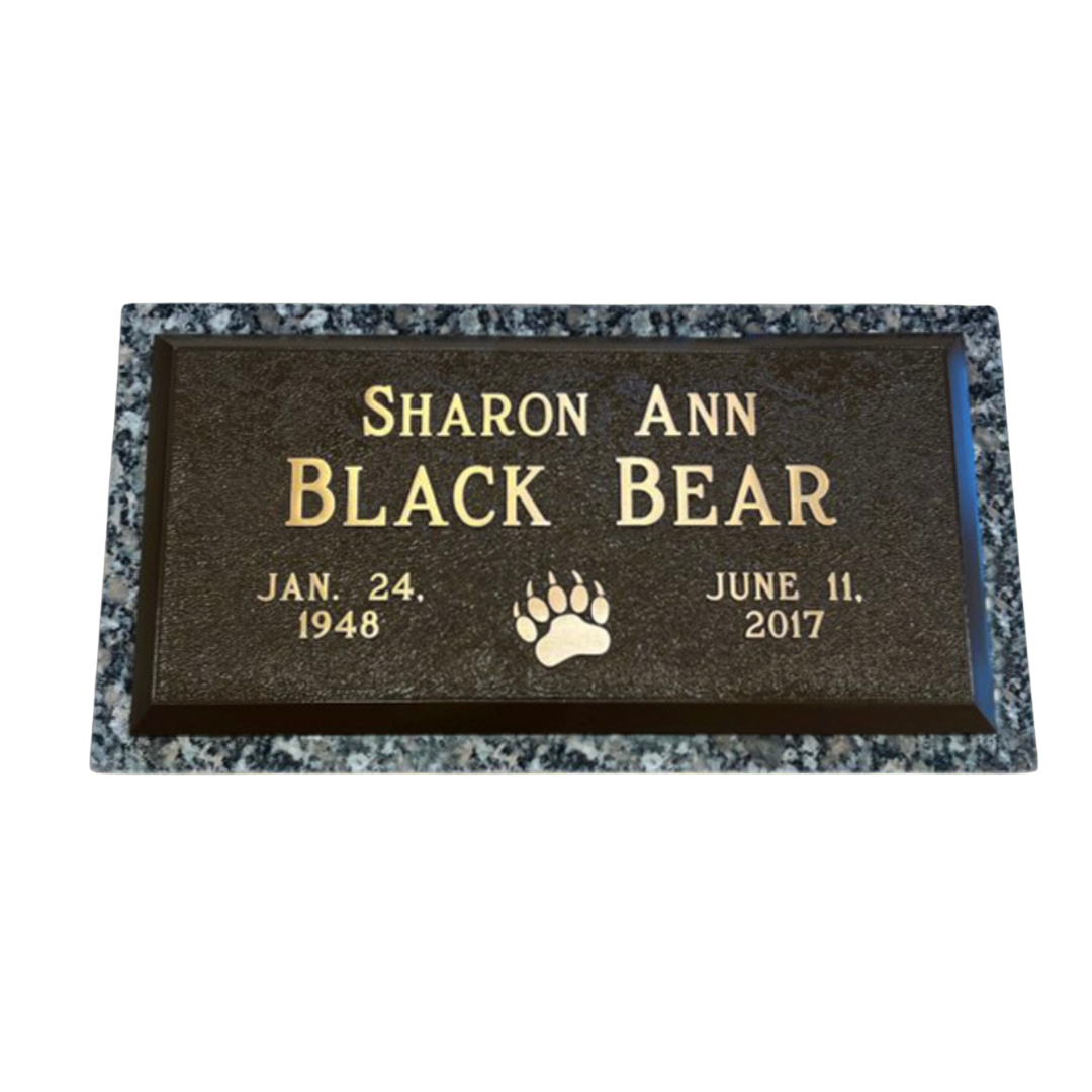 Flat bronze marker with granite surround, featuring the print of a bear.