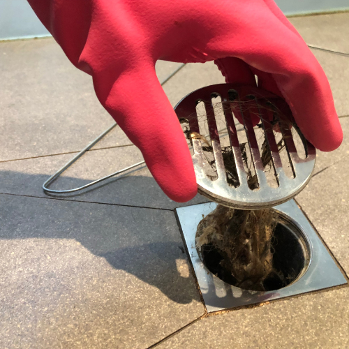 a person wearing a red glove is cleaning a drain
