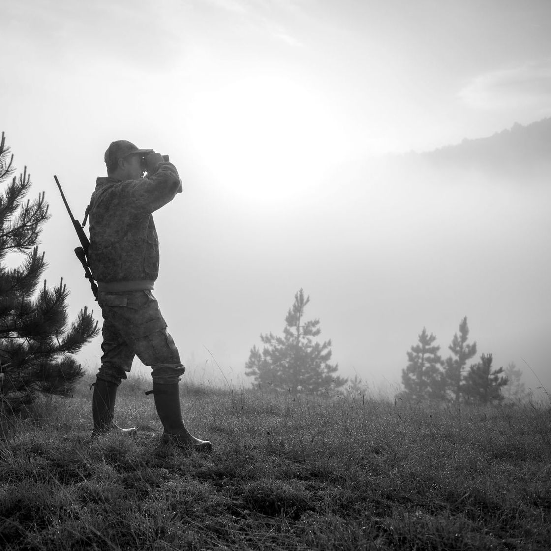 A black and white photo of a man looking through binoculars