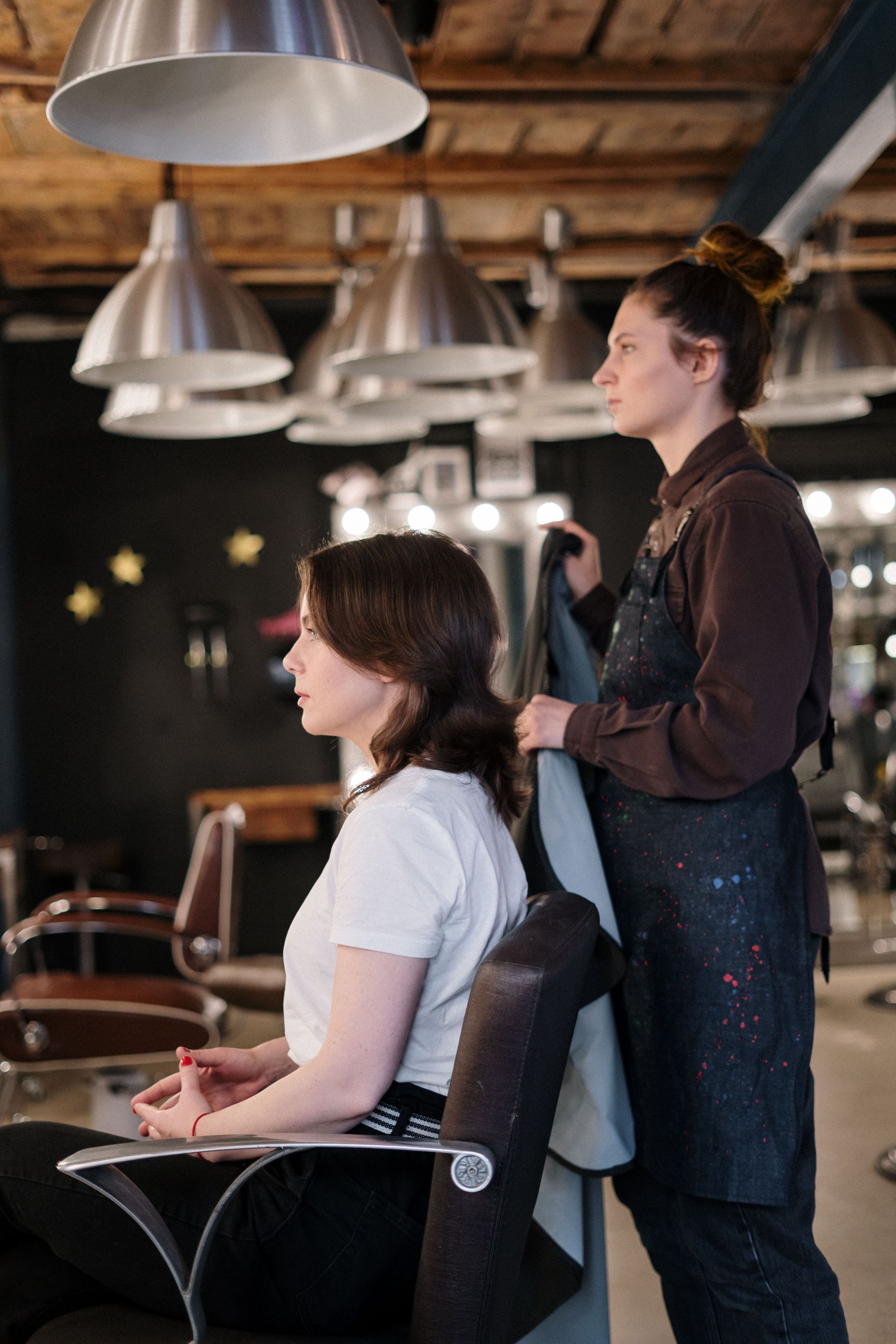 Stylist cutting a seated client’s hair in a modern salon with pendant lights.