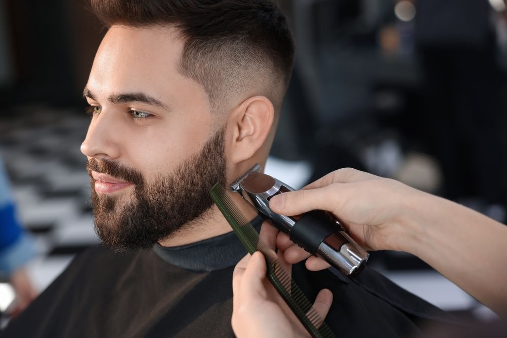 Barber trimming a man’s beard with electric clippers in a salon