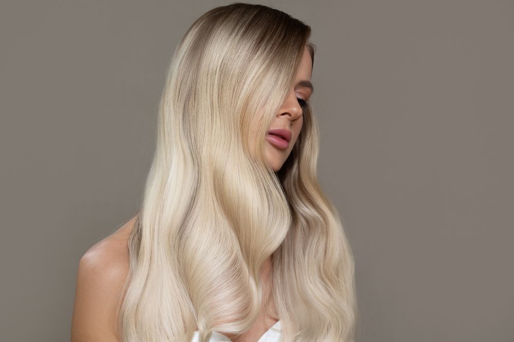 Profile of a woman with long platinum blonde hair against a plain gray background