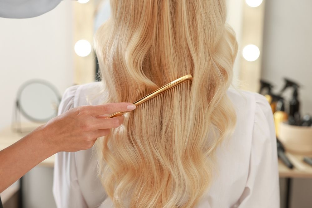 Hairdresser combing long blonde hair in a salon mirror