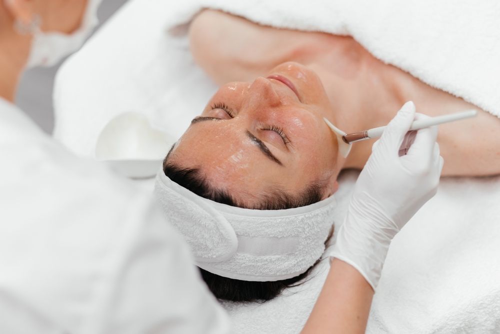 Person receiving a facial treatment with white headband and gloves in a spa setting