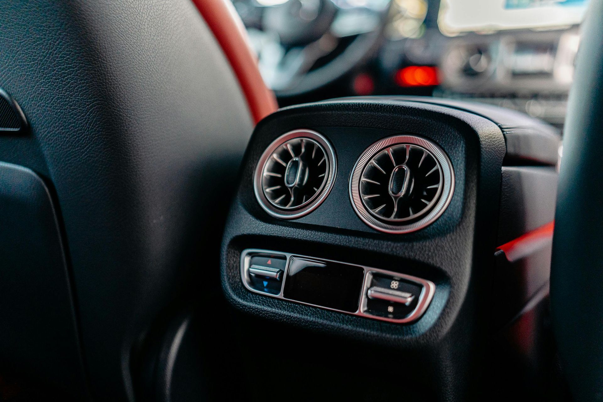 Car's rear air vents, with two circular vents and buttons, black with chrome trim. Interior shot.