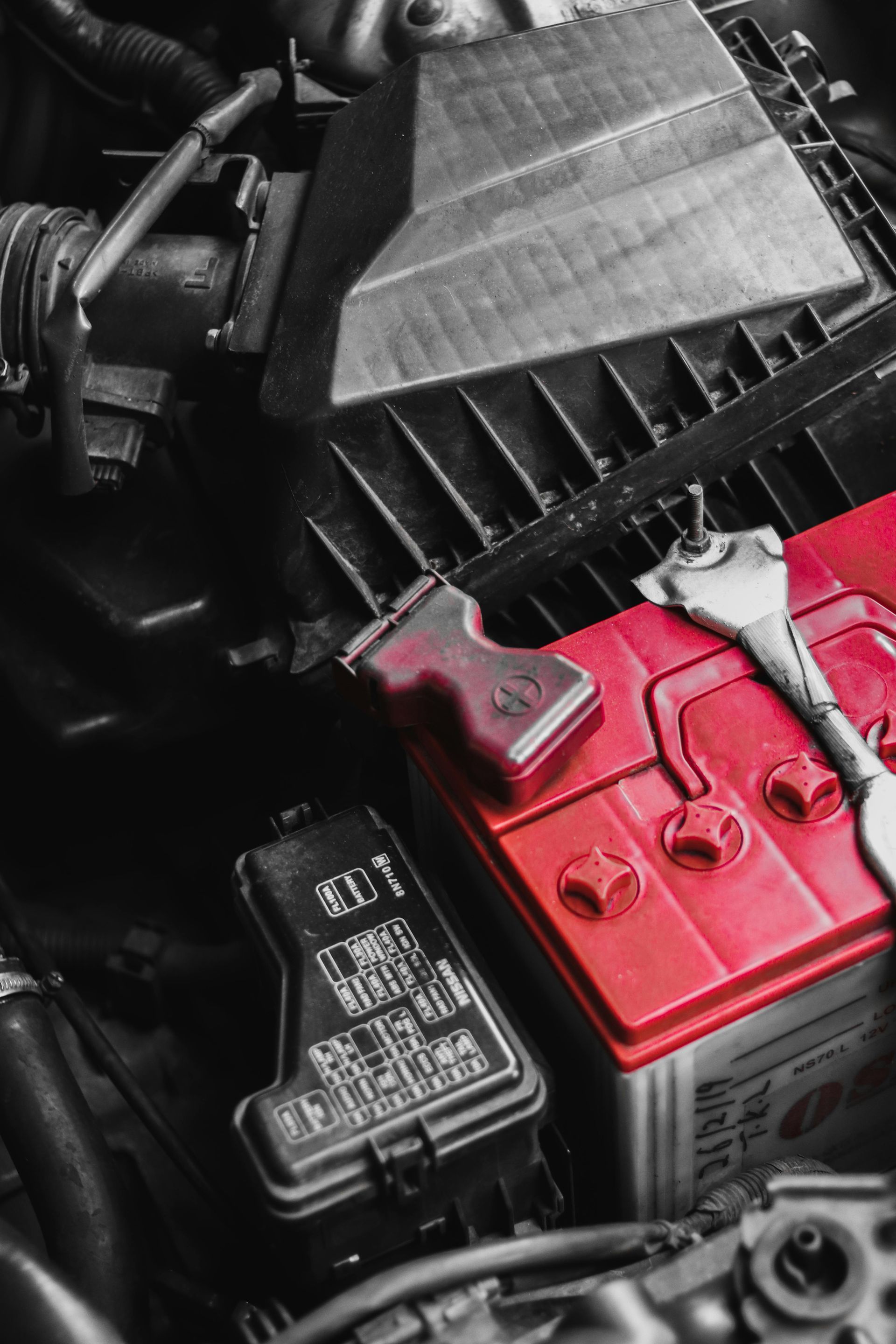 Red car battery in engine compartment with wrench.