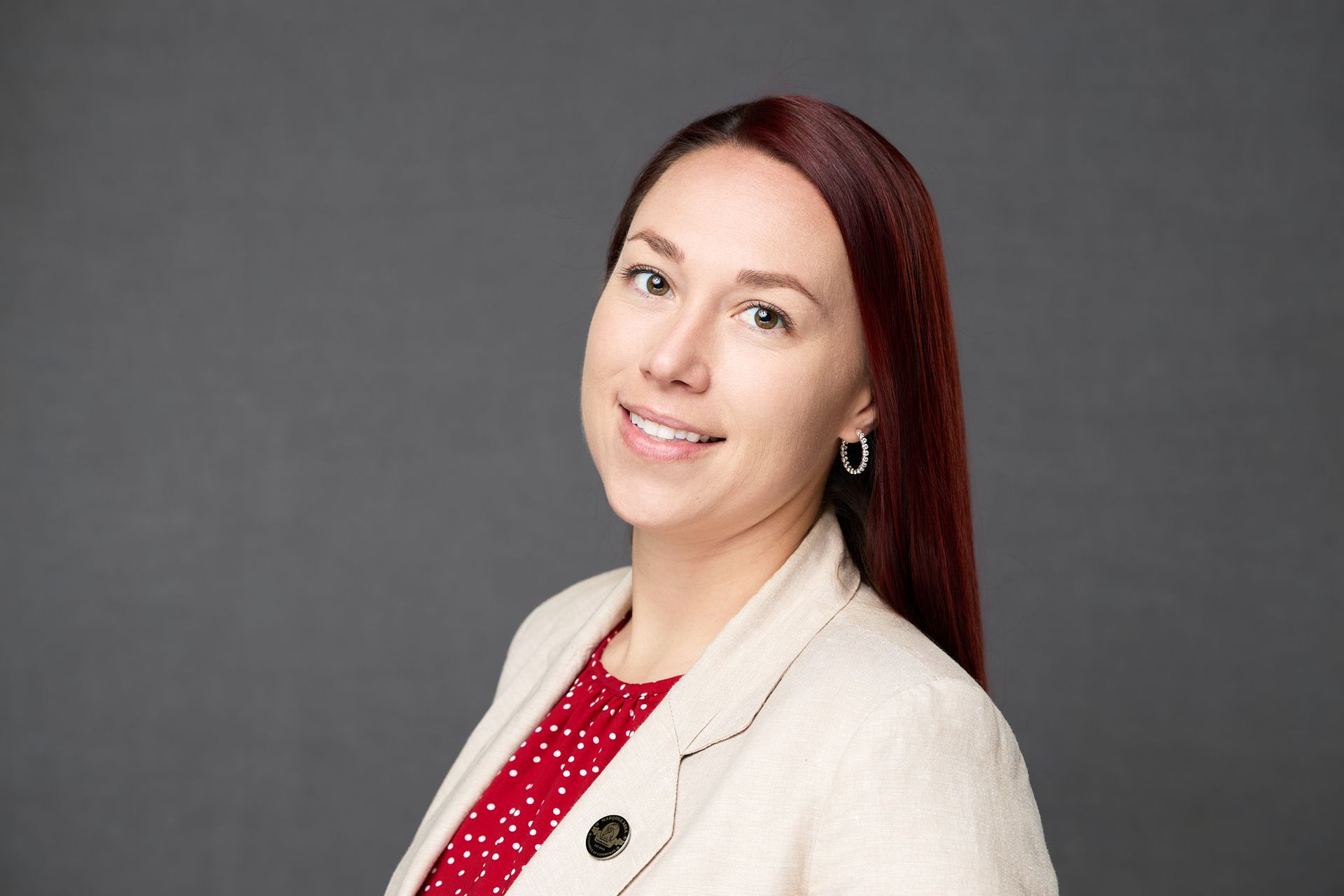 A woman with red hair is wearing a white jacket and a red polka dot shirt while posing for the camera.