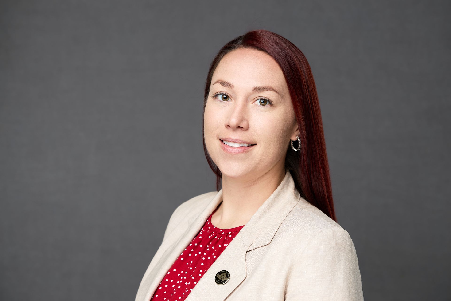 A woman with red hair is wearing a white jacket and a red polka dot shirt while posing for the camera.