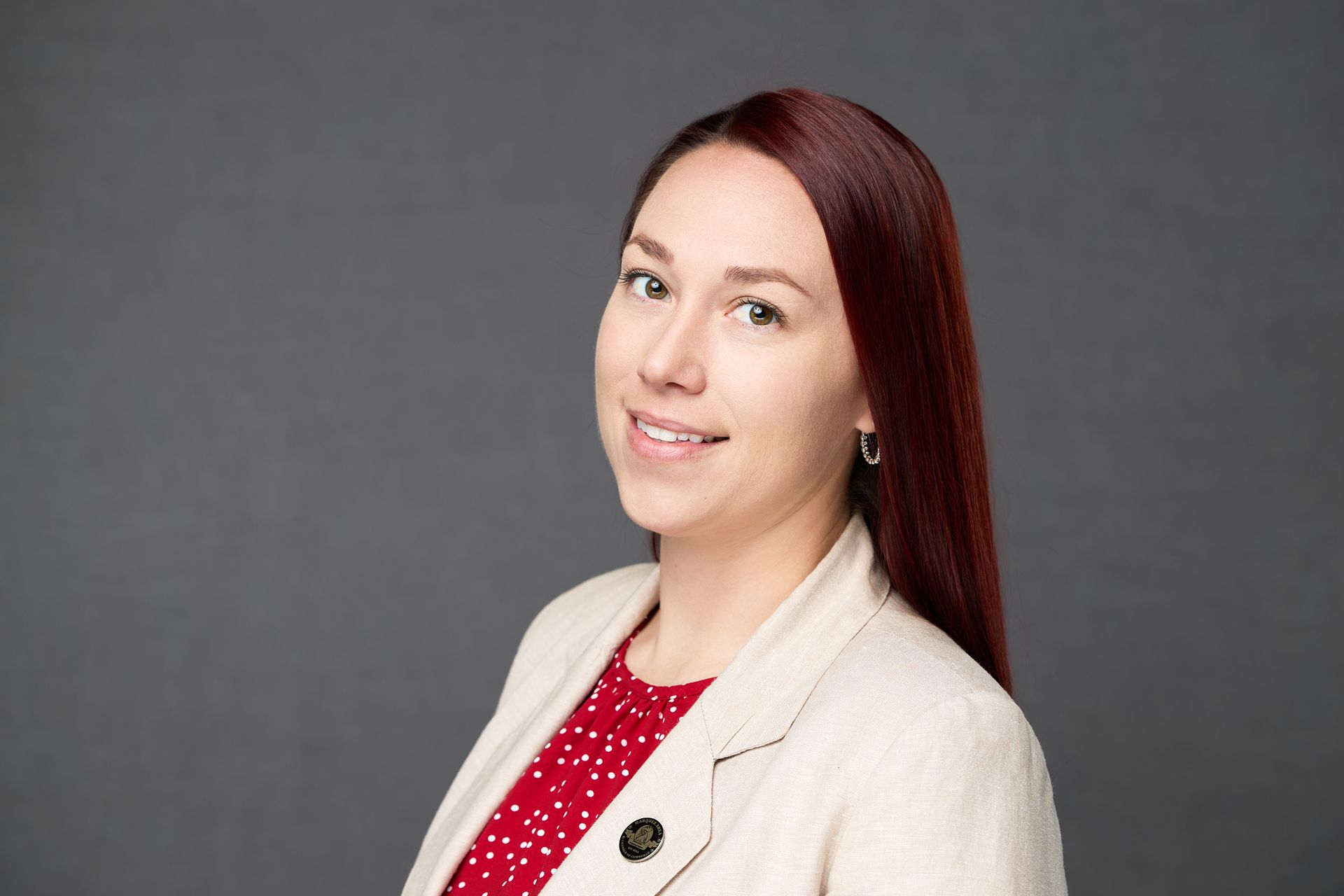 A woman with red hair is wearing a white jacket and a red polka dot shirt while posing for the camera.