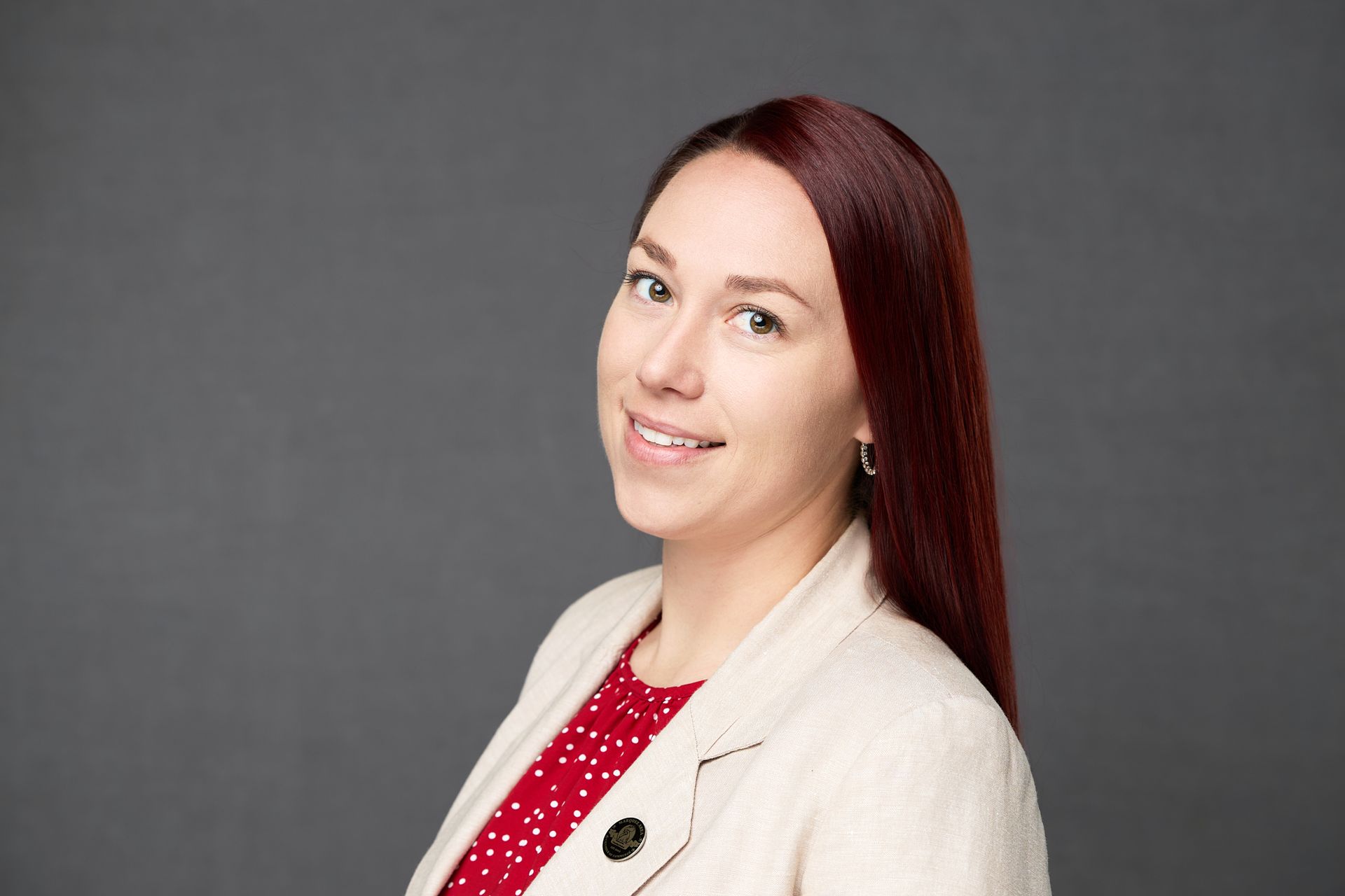 A woman with red hair is wearing a white jacket and a red polka dot shirt while posing for the camera.