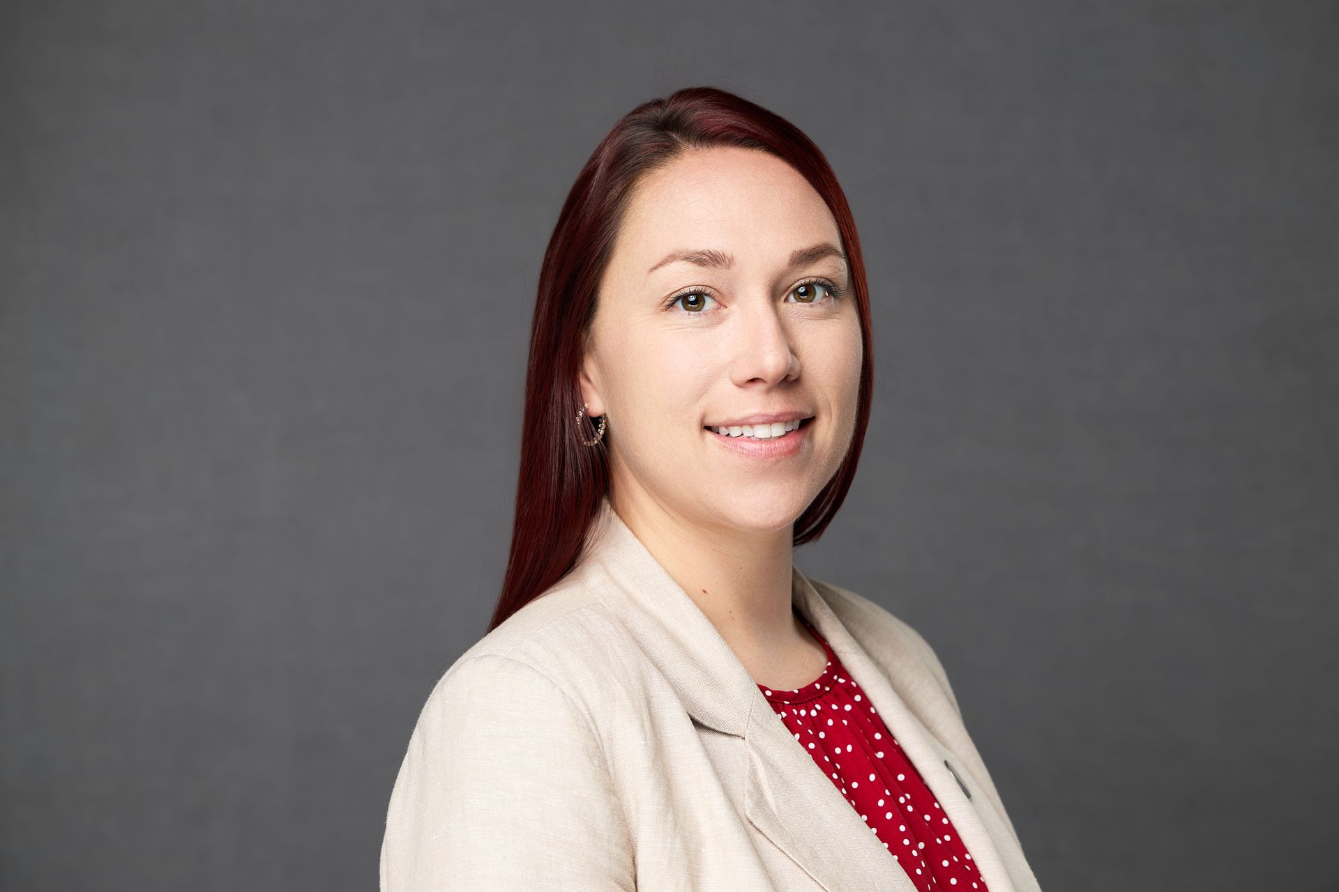 A woman with red hair is wearing a white jacket and a red polka dot shirt while posing for the camera.