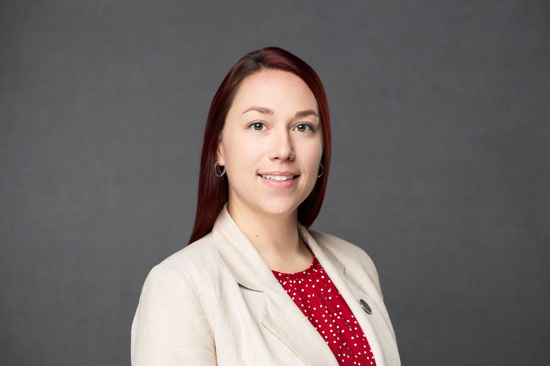 A woman with red hair is wearing a white jacket and a red polka dot shirt while posing for the camera.