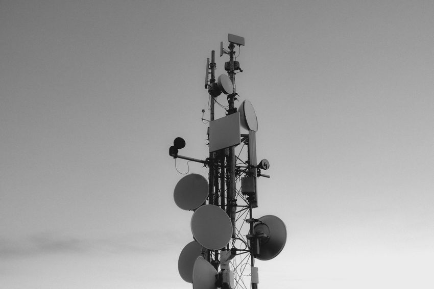 Cell tower with multiple antennas and round dishes against a clear sky