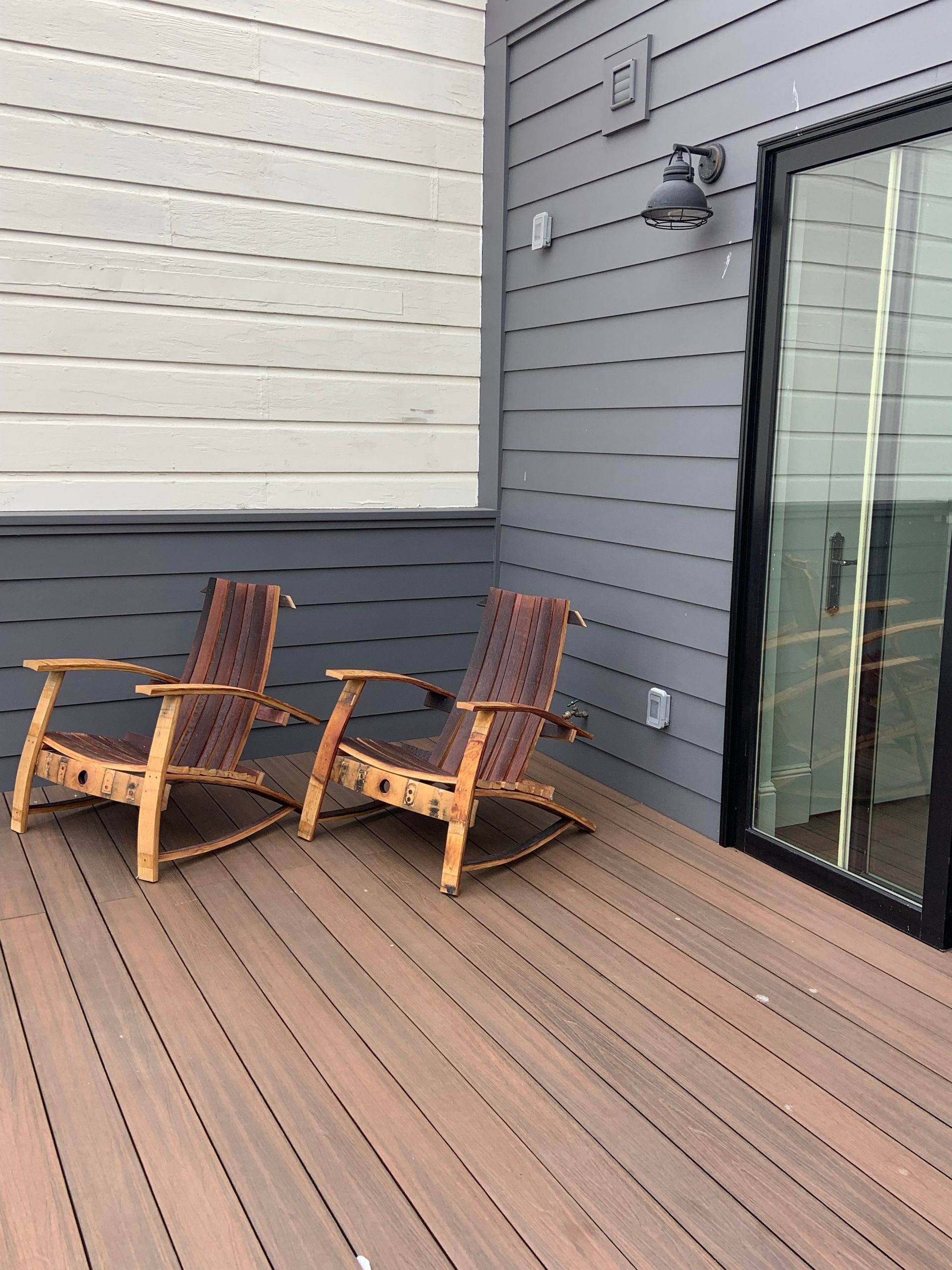 Two wooden chairs are sitting on a wooden deck next to a sliding glass door.