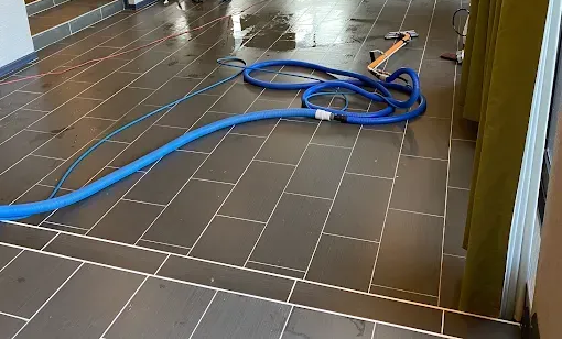 Three blue industrial fans dry a beige carpet in a living room near a fireplace.