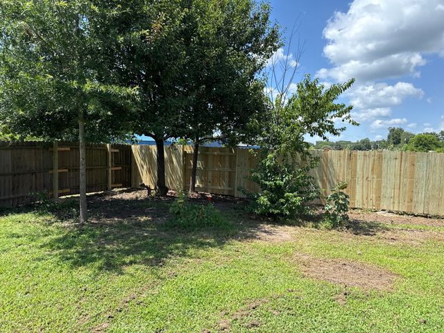 Backyard with grass, trees, wooden fence, and a partly cloudy blue sky