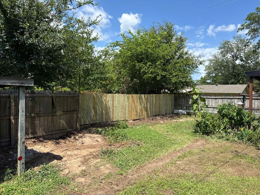 Backyard with wooden fence, grassy lawn, trees, and a small shed under a sunny blue sky