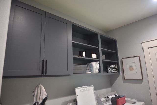 Gray wall cabinets above a desk with shelves and office supplies in a home office.