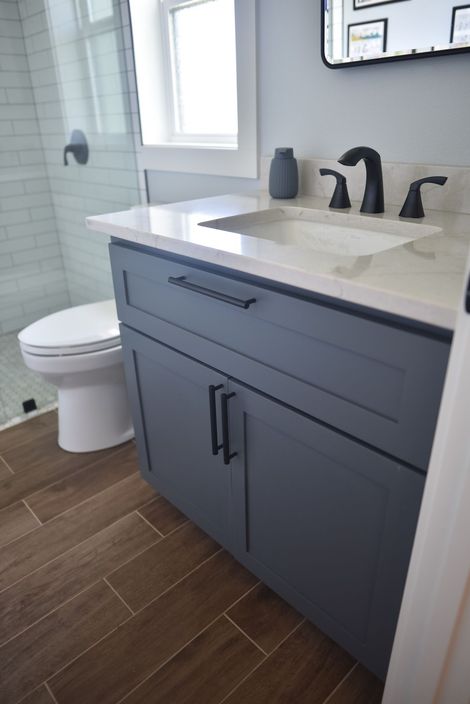 Modern bathroom vanity with gray cabinet, white countertop, black faucet, toilet, and tiled floor
