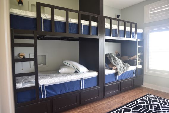 Children’s bunk beds in a bright bedroom with blue bedding and a window seat.