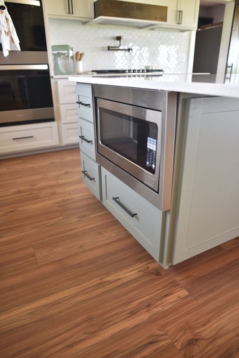 Modern kitchen island with built-in microwave, white cabinetry, and wood flooring