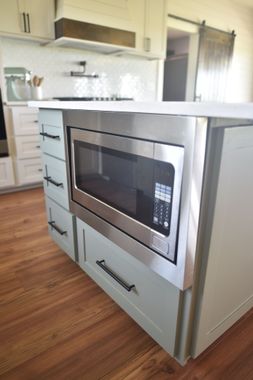 Kitchen island with built-in stainless steel microwave and light gray drawers on a wood floor.