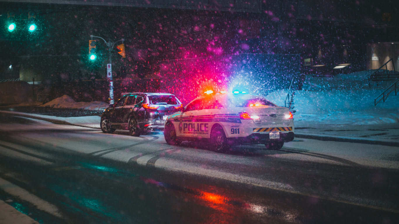 A police car is driving down a snowy street at night due to a car accident