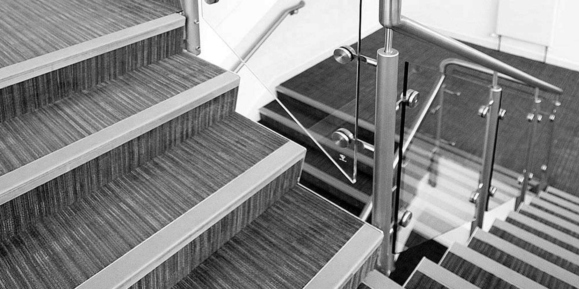 Staircase with wooden steps and a glass and metal railing, viewed from above.