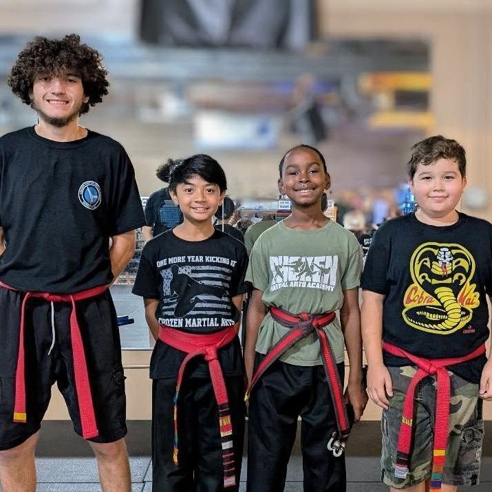 A man is kneeling down next to a young boy in a taekwondo class.